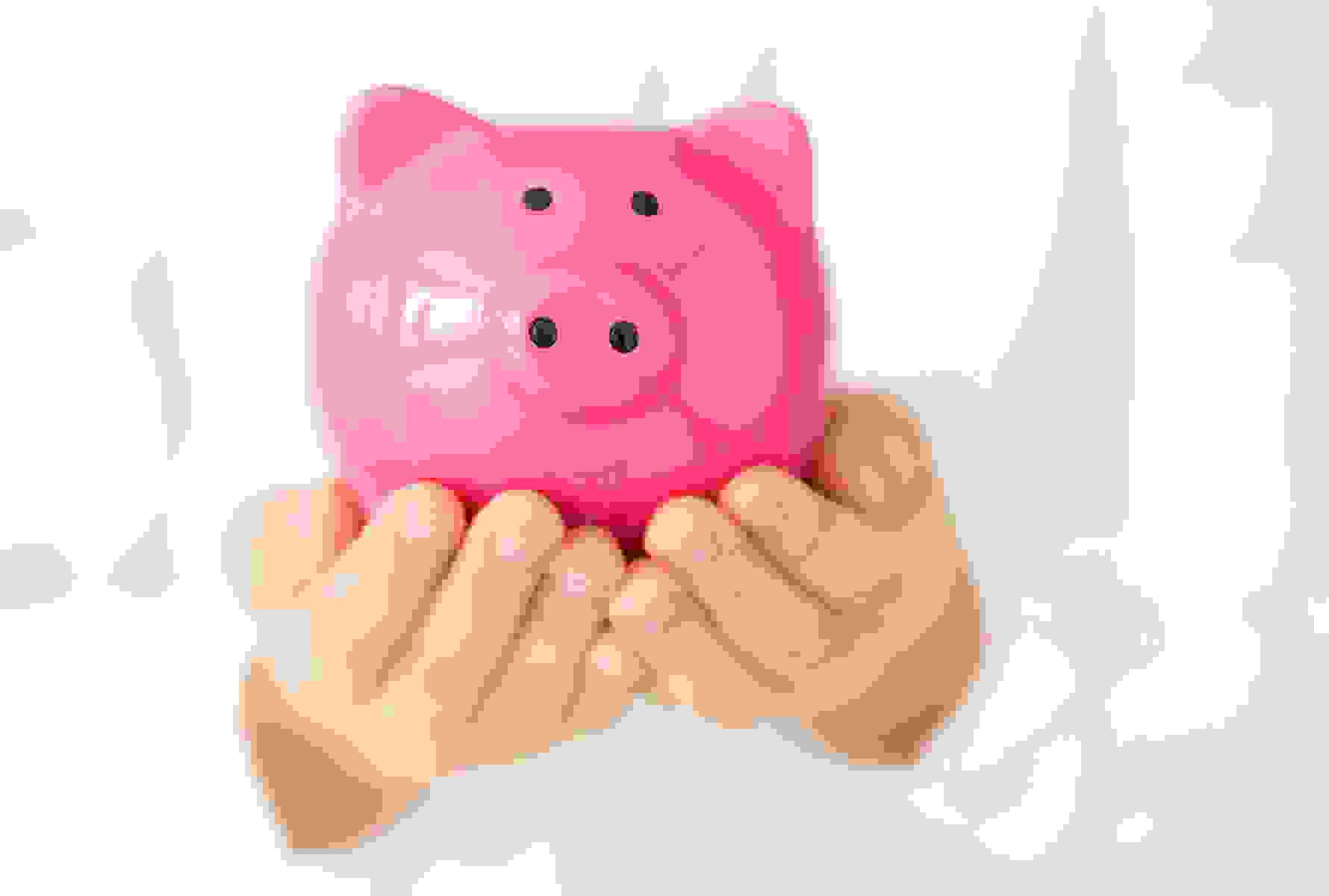 Deux mains ouvertes tiennent une tirelire rose – un symbole de gestion responsable des cotisations et de financement transparent.