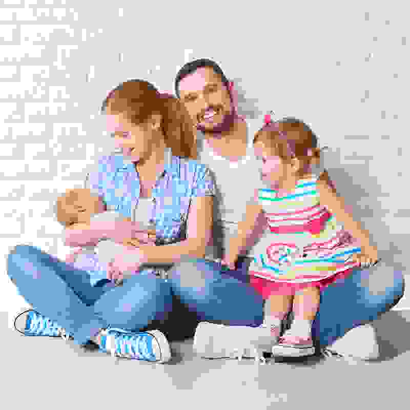 Eine junge Familie sitzt auf dem Boden vor einer weissen Wand – zur Geburt oder Adoption erhalten Sie unter bestimmten Voraussetzungen CHF 400.– als Geschenk.