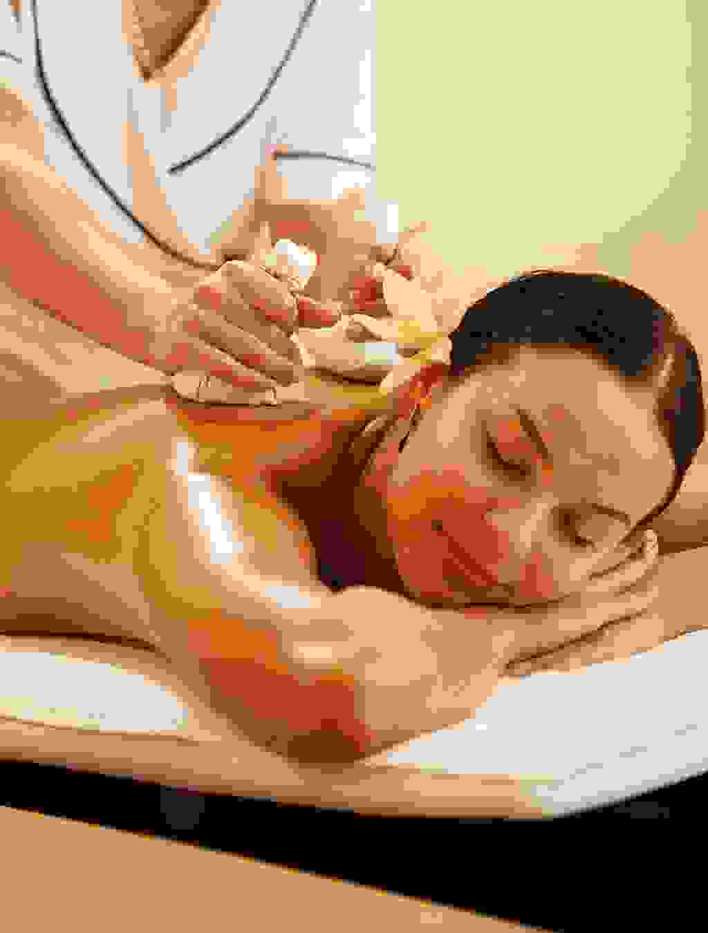 Bildbeschreibung: Eine schwangere Frau liegt entspannt auf dem Bauch und erhält eine Massage mit duftenden Kräutersäckchen – ein wohltuendes Verwöhnprogramm für werdende Mütter.