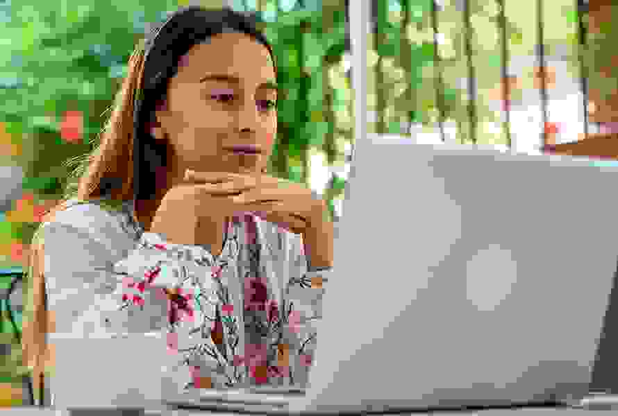 Una giovane donna è seduta rilassata sul balcone e utilizza il formulario online – veloce e comodo.