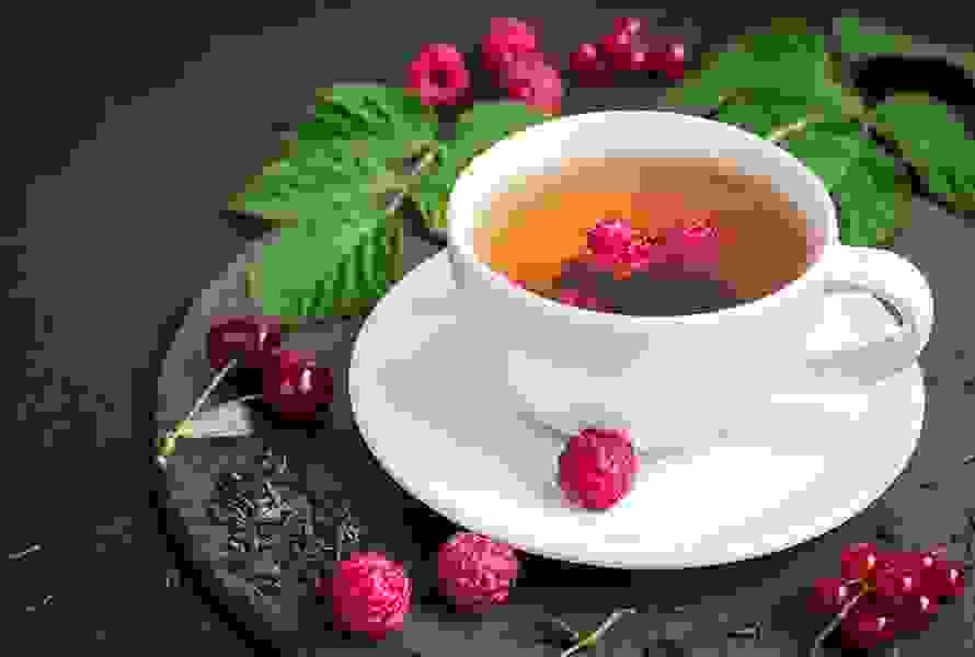 Eine Tasse mit Himbeerblättertee, frischen und getrockneten Blättern sowie Himbeeren – ein natürlicher Begleiter zur Geburtsvorbereitung.