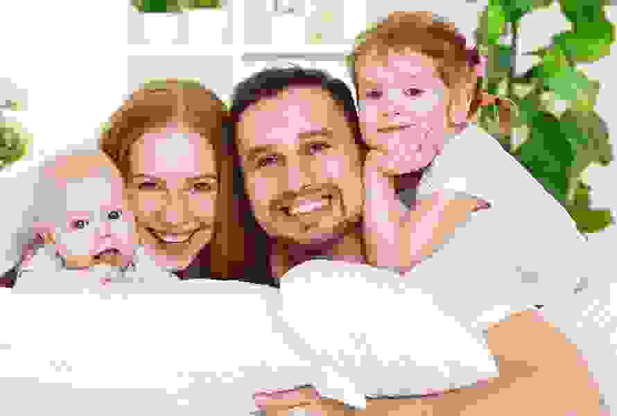 Una famiglia allegra guarda direttamente nella fotocamera dal divano – per tutte le vostre domande sulla Soluzione cassa malati.