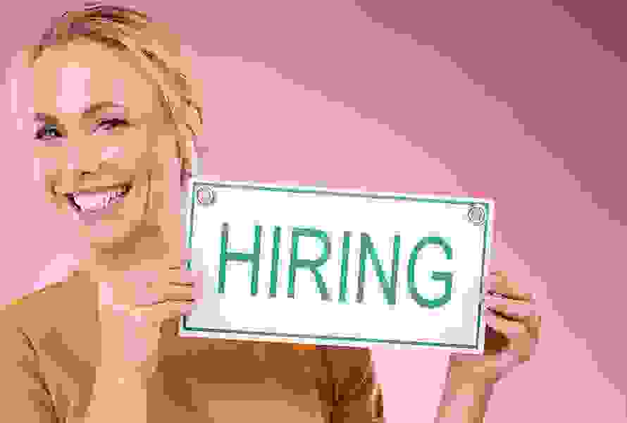 Eine Frau hält ein Schild mit „Hiring“ in die Höhe. Bei PRO LIFE arbeiten bedeutet: Sinnvolle Aufgaben übernehmen und Teil einer engagierten Gemeinschaft sein.
