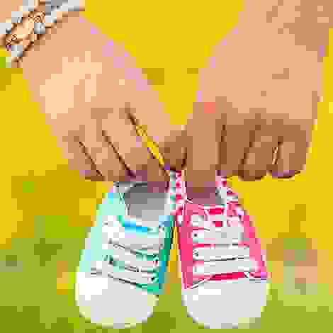 Zwei Hände halten Babyschuhe in Rosa und Hellblau – ein Symbol für Mehrlingsfreuden und die bevorstehende Geburt.