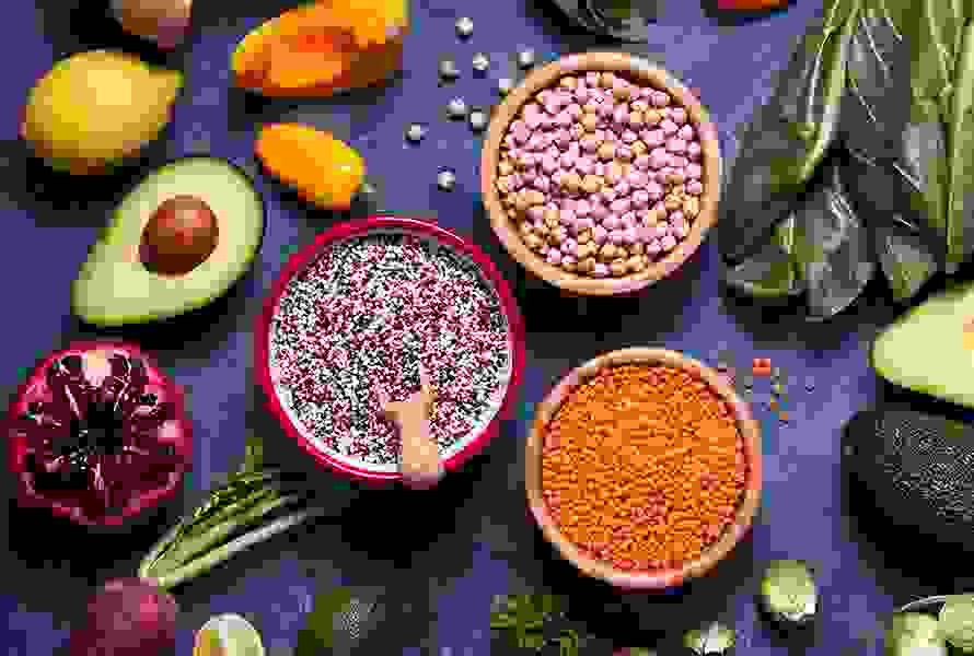 Getrocknete Kichererbsen, rote Linsen, Quinoa, Kürbis, Avocado, Peperoni, Granatapfel und Krautstiele – perfekte Zutaten für eine nährstoffreiche vegetarische Ernährung.