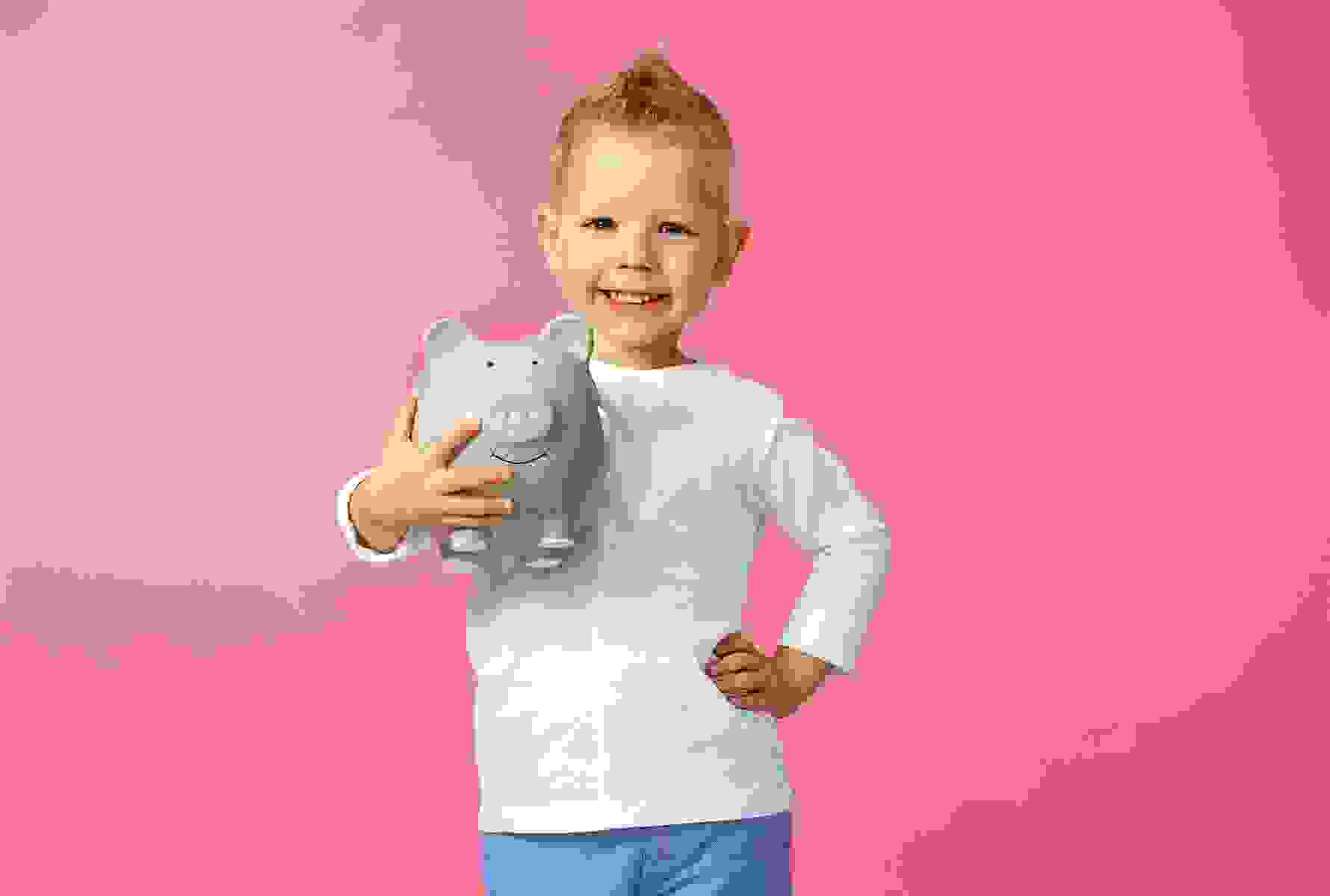 Ein Junge mit einem Sparschwein im Arm steht vor einem dunkelrosaroten Hintergrund.