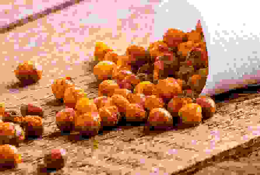 Des pois chiches dorés roulent hors d’un sachet en papier ouvert sur une table en bois rustique. Une collation saine et riche en fibres – croquante, aromatique et facile à préparer soi-même.

