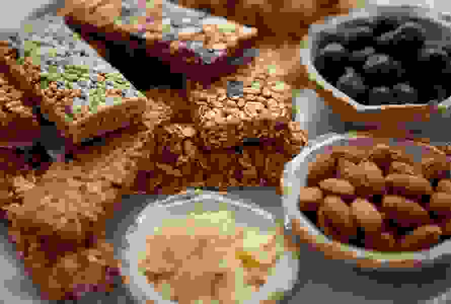 Varie barrette ai cereali fatte in casa su un piatto, accanto a ciotoline con mirtilli, mandorle e lamelle di mandorle – la fonte di energia perfetta.

