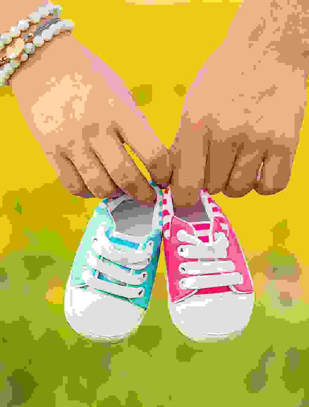 Zwei Hände halten Babyschuhe in Rosa und Hellblau – ein Symbol für Mehrlingsfreuden und die bevorstehende Geburt.
