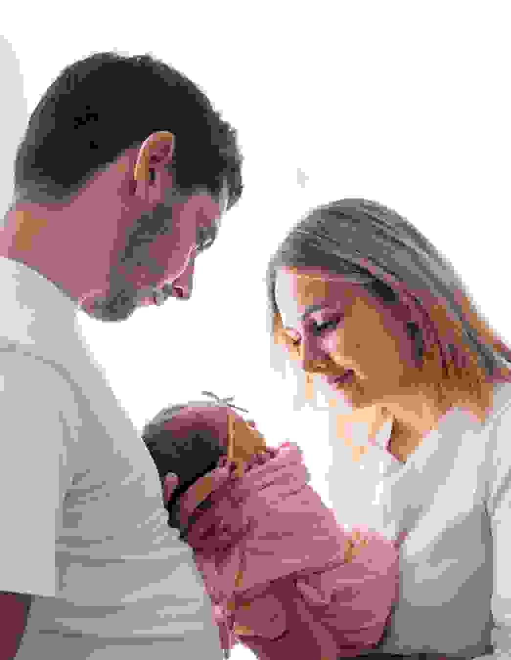 Ein glückliches Paar schaut liebevoll auf das Neugeborene in den Armen der Mutter – ein emotionaler Moment nach einer langen Reise voller Vorfreude und Geduld.