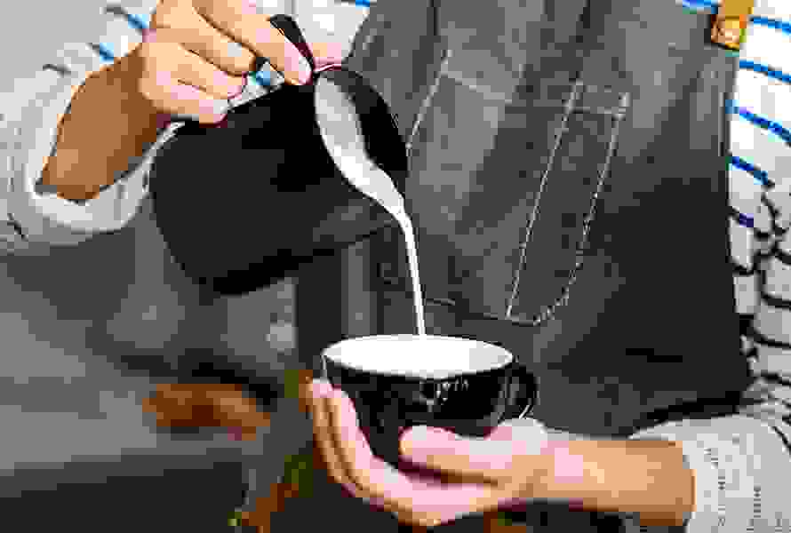 Eine Barista arbeitet konzentriert beim beim Eingiessen der Milch – kleine Genussmomente helfen beim Durchatmen im Alltag.