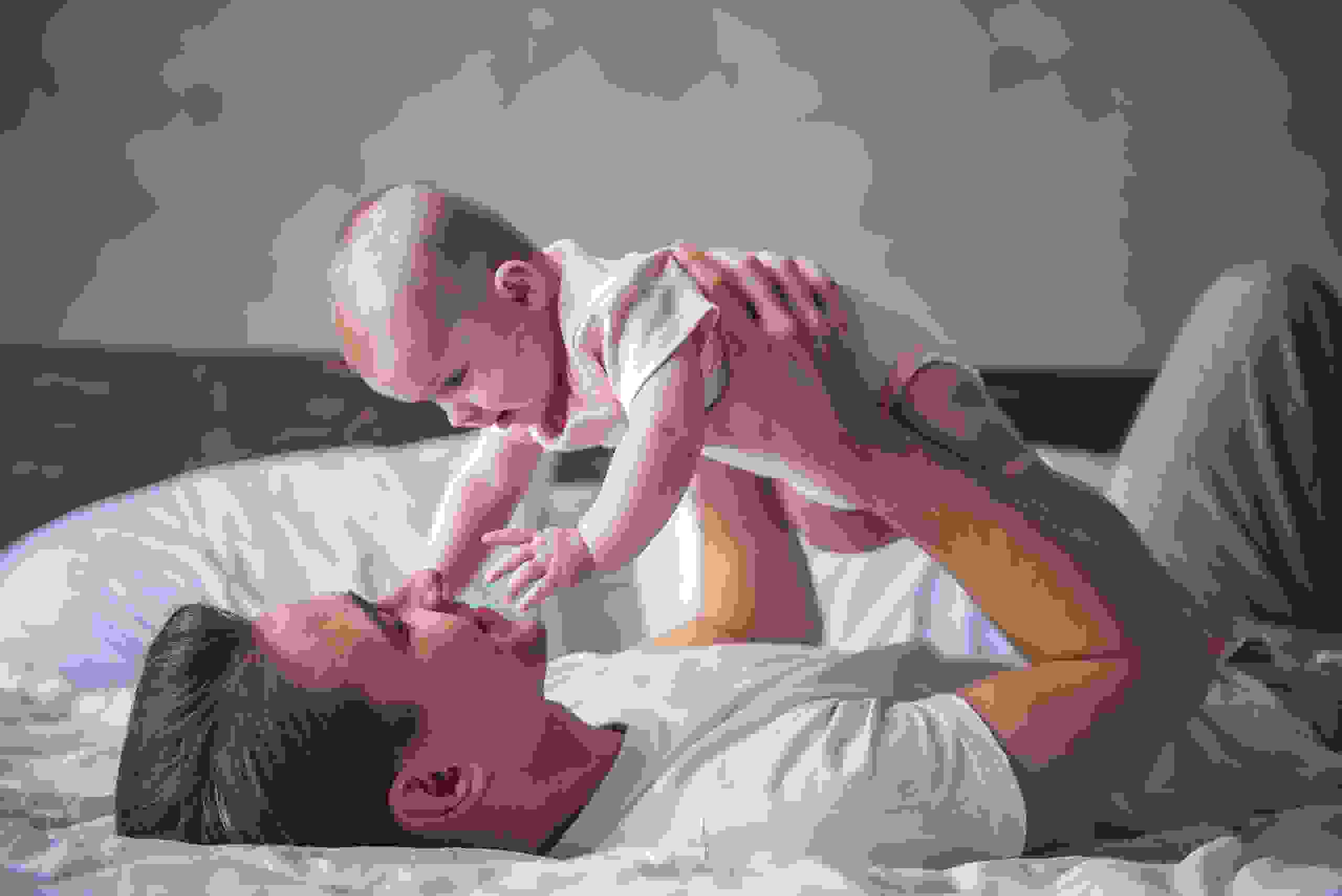 Un giovane padre è sdraiato sulla schiena, rilassato, e tiene teneramente il figlio sopra di sé – un’immagine di sicurezza e vicinanza.