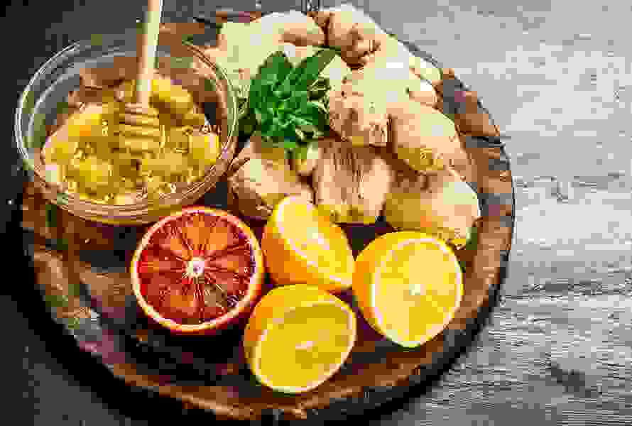 Auf einem Holzbrett liegen frischer Ingwer, Honig, Zitronen und eine Blutorange – bewährte Hausmittel gegen Schwangerschaftsübelkeit, voller Vitamine und Mineralstoffe.