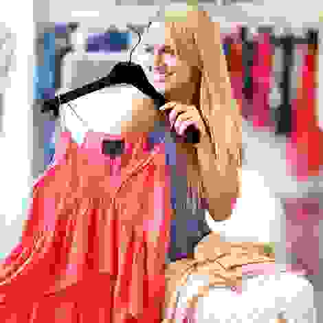 Blonde Frau hält ein rotes Trägerkleid hoch, zeigt die Freude über bequeme und stylische Umstandsmode in der 14. Schwangerschaftswoche.