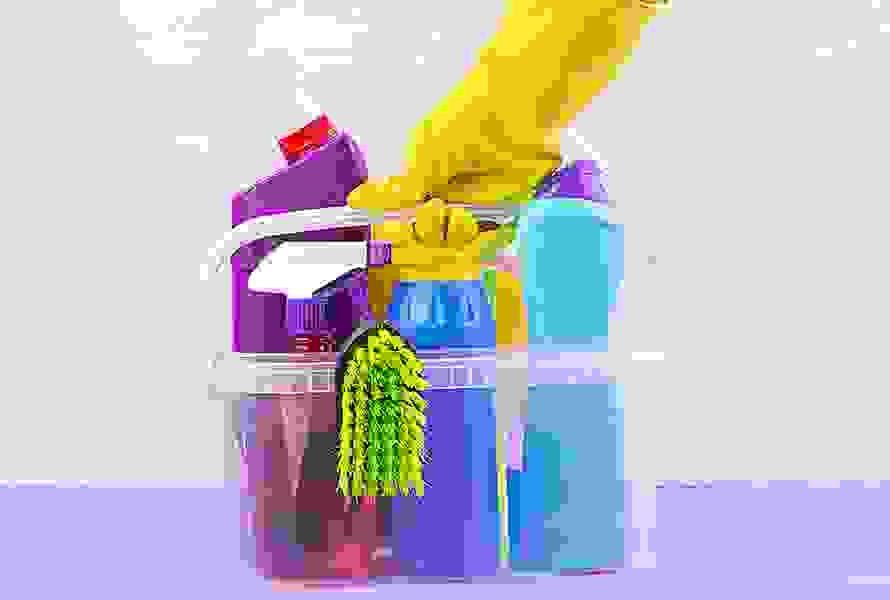 Ein Putzeimer mit Reinigungsmitteln und Bürste wird von einer Hand in Gummihandschuh gehalten – ein Symbol für Unterstützung durch Spitex oder Haushaltshilfe.
