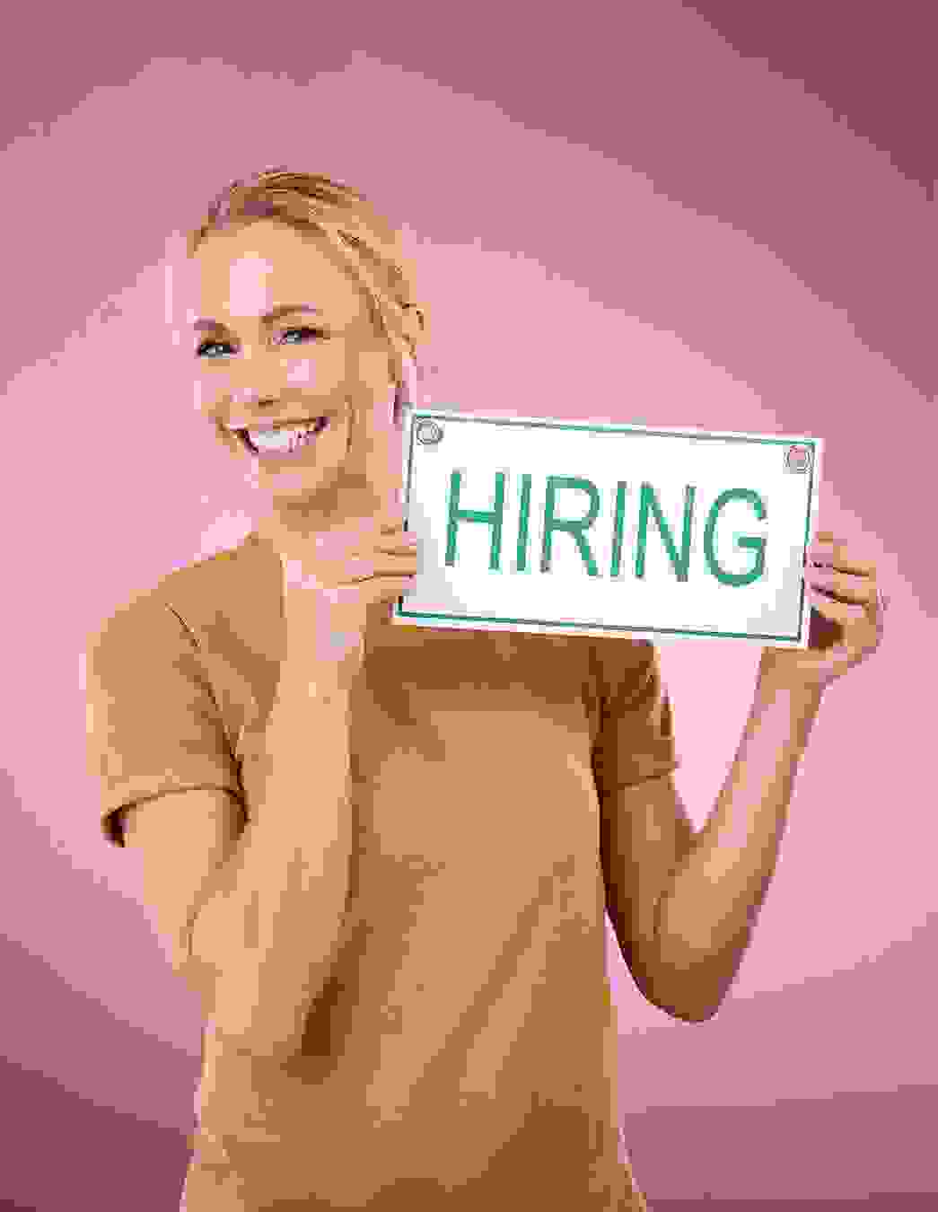 Una giovane donna solleva un cartello con la scritta «Hiring» – un segno di apertura e curiosità verso nuovi talenti che condividono i nostri valori e desiderano contribuire attivamente.