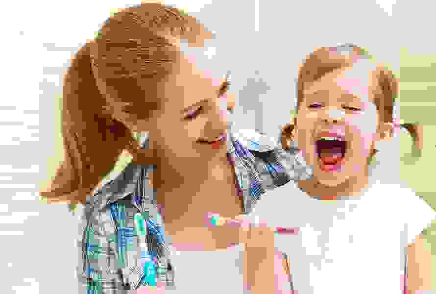Liebevolle Szene, in der eine Mutter ihrer kleinen Tochter beim Zähneputzen unterstützt – ein wichtiger Schritt für gesunde Zähne und Vorsorge.