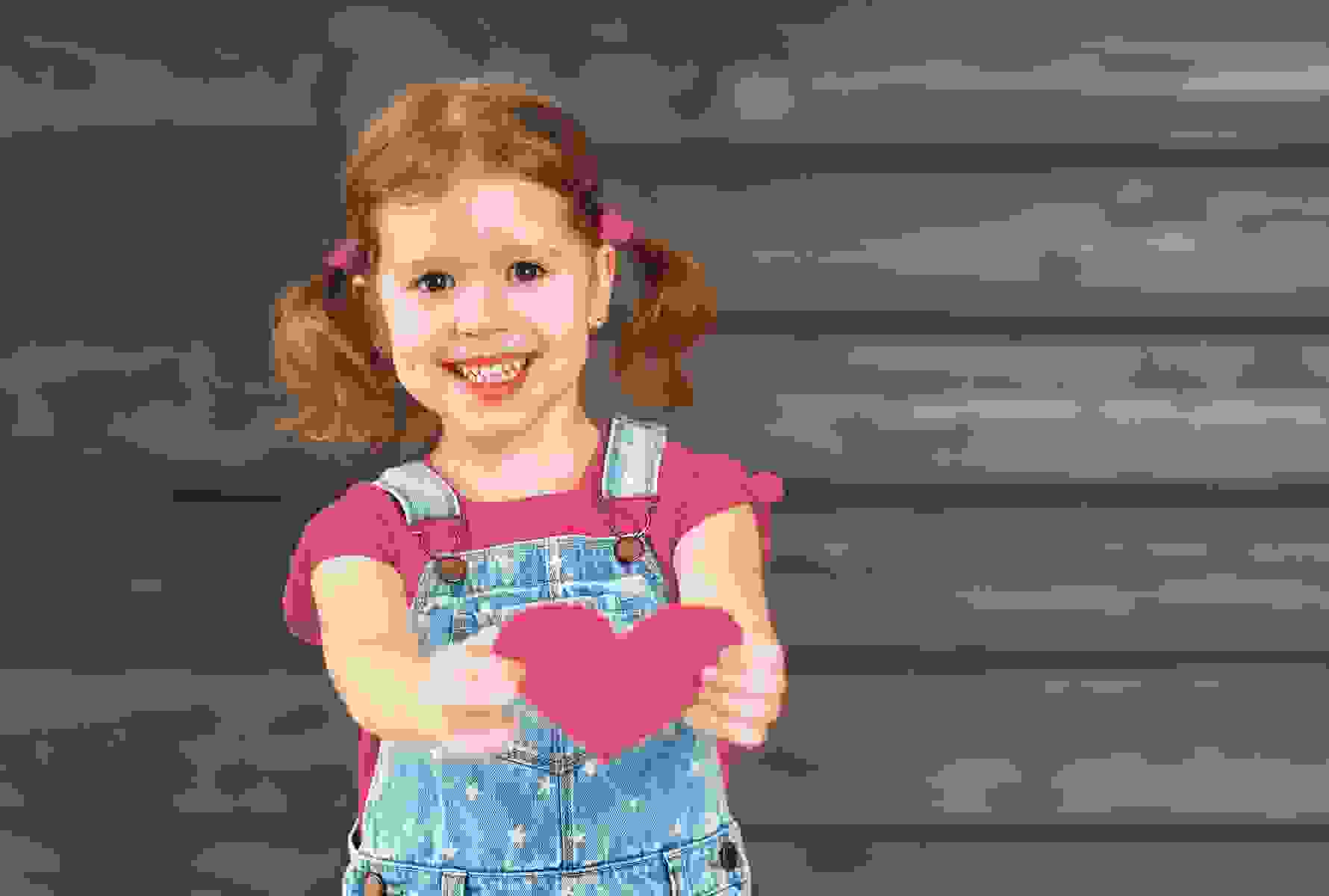 Una bambina porge un cuore verso la fotocamera – un simbolo forte di amore, cura e umanità.