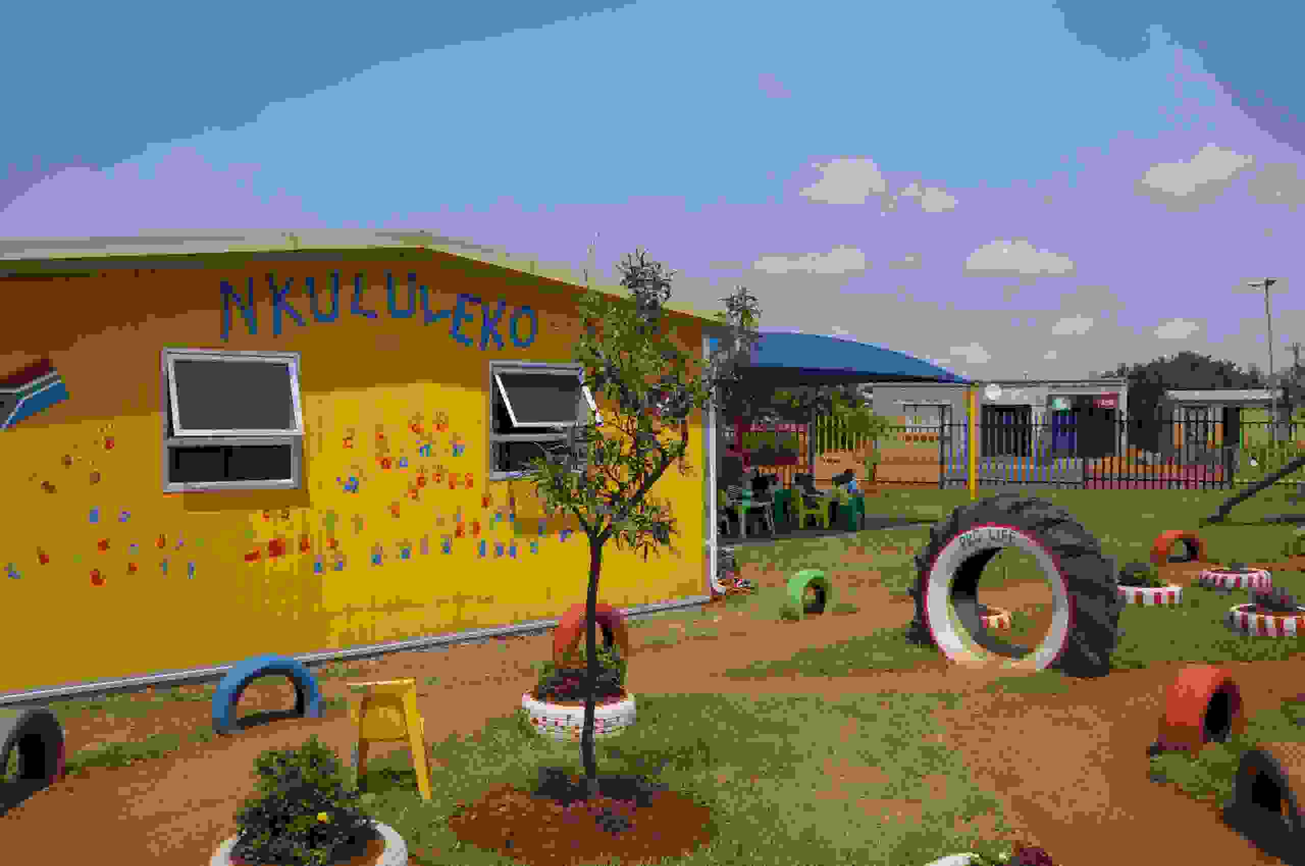 Das neue Kita-Gebäude mit Spielplatz und Sonnenschirm – ein Ort, an dem Kinder geschützt spielen, lernen und sich entfalten können.