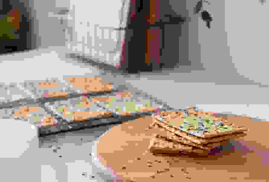 Frisch gebackene Knäckebrotscheiben kühlen auf einem Gitter aus, im Vordergrund liegen einige Scheiben auf einem Holzbrett. Der ballaststoffreiche Snack für jede Tageszeit – pur oder belegt.