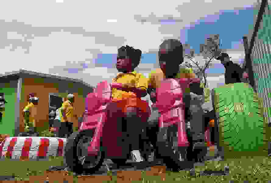 Zwei Kinder fahren lachend auf pinken Plastiktöffs durch den Garten der KITA – unbeschwerte Momente in sicherer Umgebung.