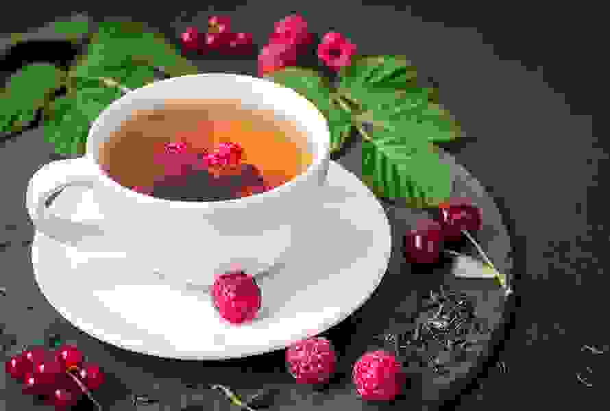 Eine Tasse Himbeerblättertee, umgeben von frischen und getrockneten Himbeerblättern sowie Himbeeren – ein bewährtes Hausmittel in den letzten Schwangerschaftswochen.