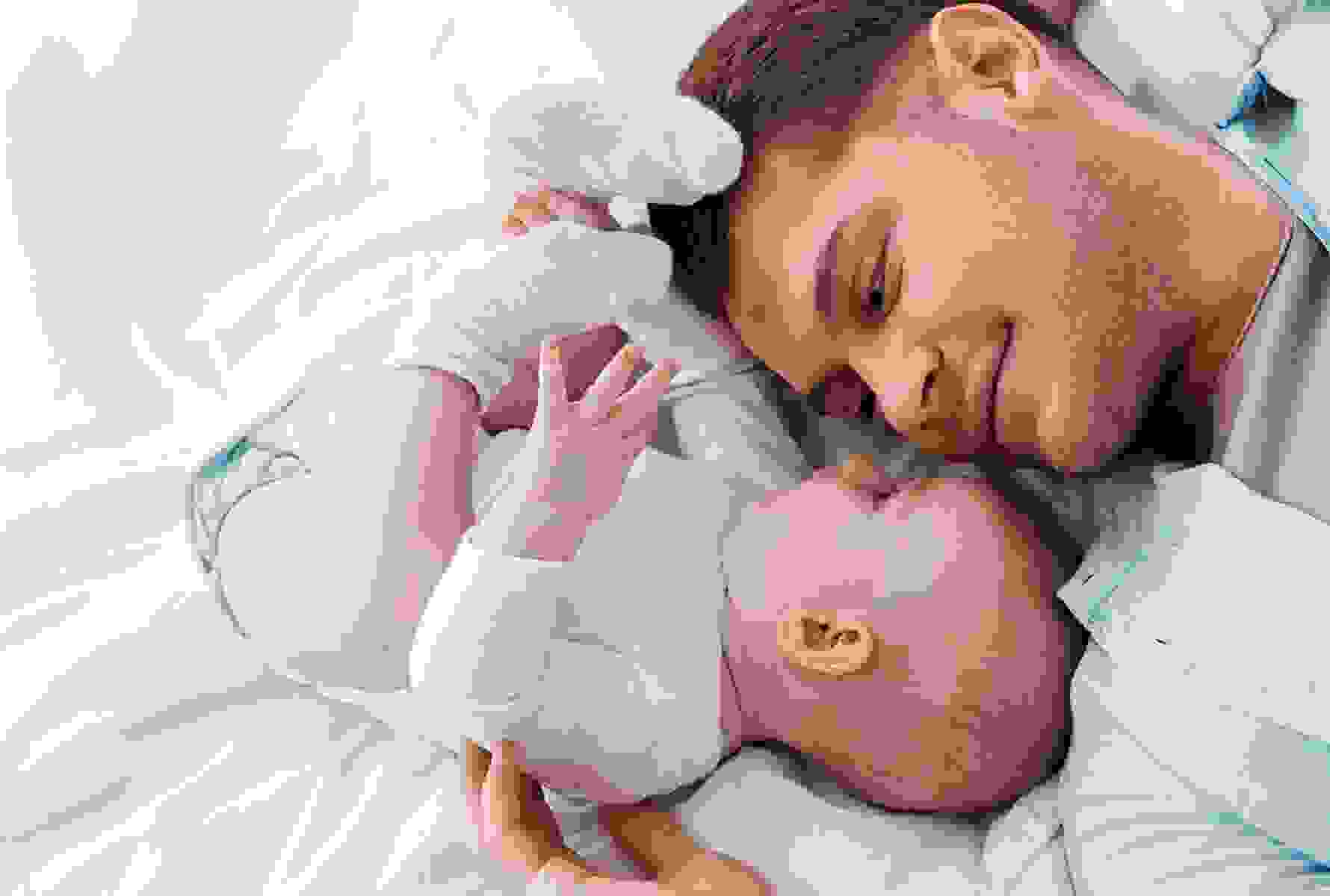 Un padre sdraiato a faccia a faccia con il suo bambino sul letto – un momento intimo che mostra ciò per cui PRO LIFE si impegna: vicinanza, famiglia, umanità.