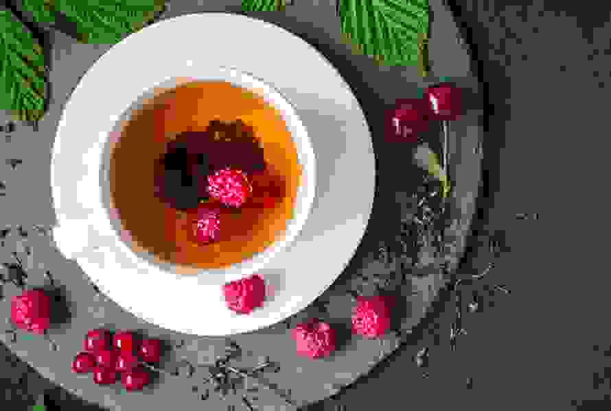 Eine Tasse Himbeerblättertee zwischen frischen und getrockneten Himbeerblättern – in dieser Woche wird der Tee abgesetzt, doch im Wochenbett kann er weiterhin hilfreich sein.