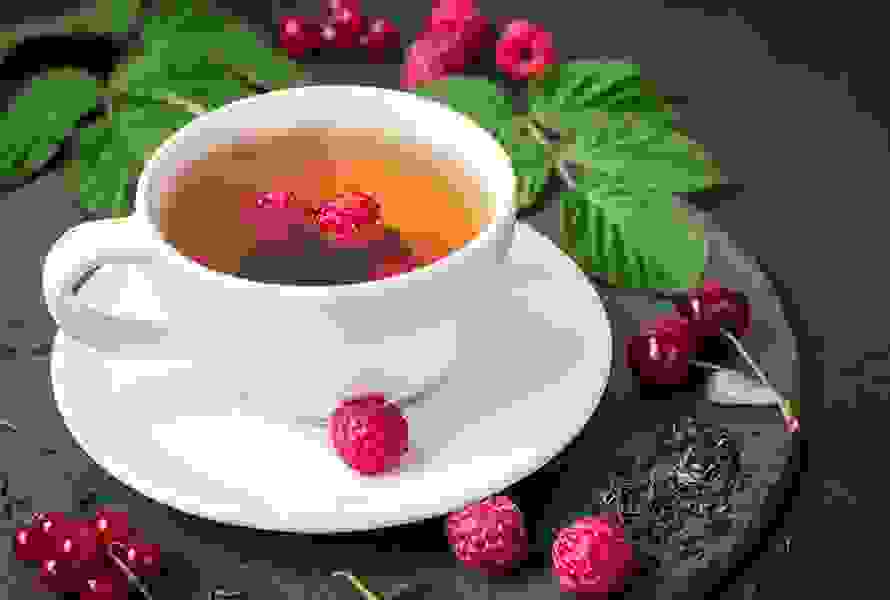 Eine Tasse Himbeerblättertee mit frischen und getrockneten Himbeerblättern – beliebt zur Geburtsvorbereitung, aber in dieser Woche ist eine kurze Einnahmepause empfohlen.