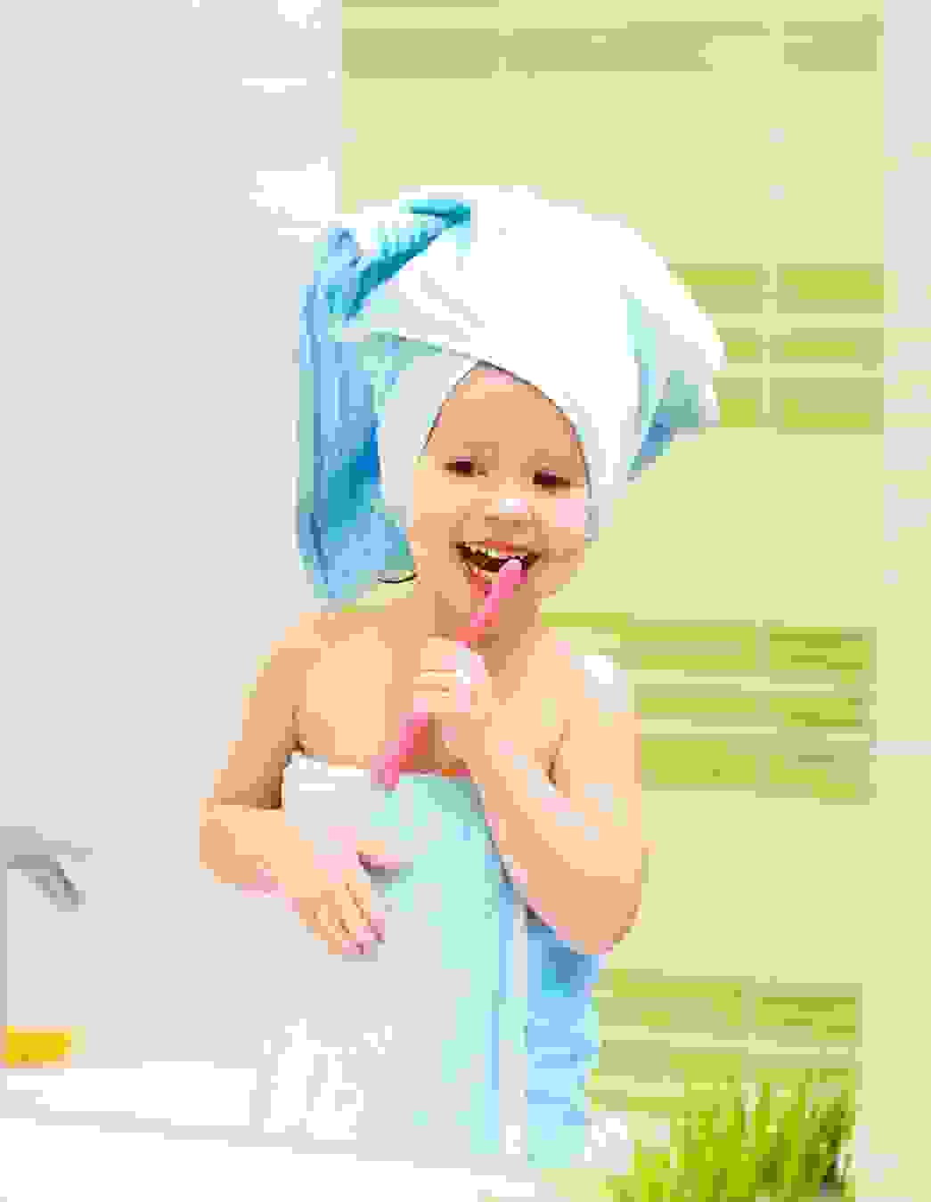 Ein kleines Mädchen mit Handtuch auf dem Kopf putzt sich konzentriert die Zähne – ein Bild für einen gesunden Start ins Leben mit Unterstützung von PRO LIFE.