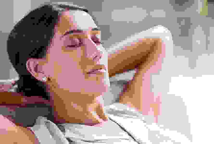 Eine dunkelhaarige Schwangere sitzt entspannt auf dem Sofa – bewusste Pausen sind jetzt besonders wichtig, um Kraft zu tanken.