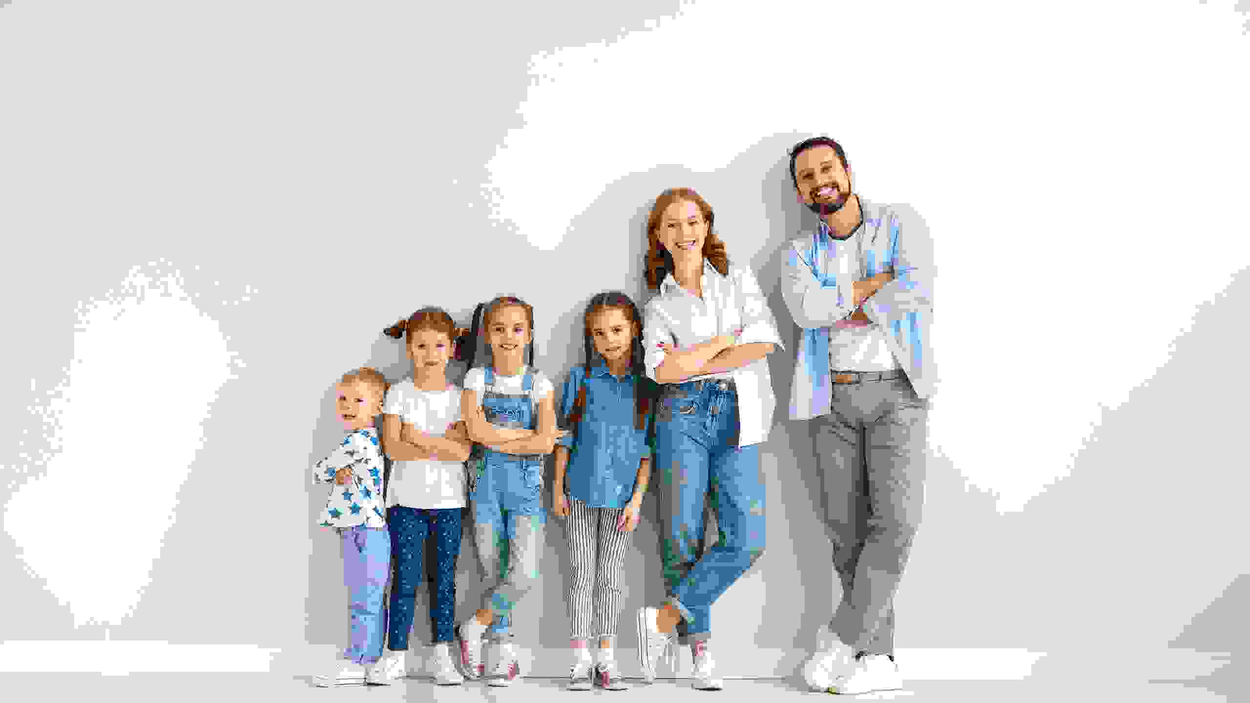 Ein Elternpaar mit vier Kindern steht entspannt an eine graue Wand gelehnt – ein Bild für Zusammenhalt, Vertrauen und das, was wirklich zählt.