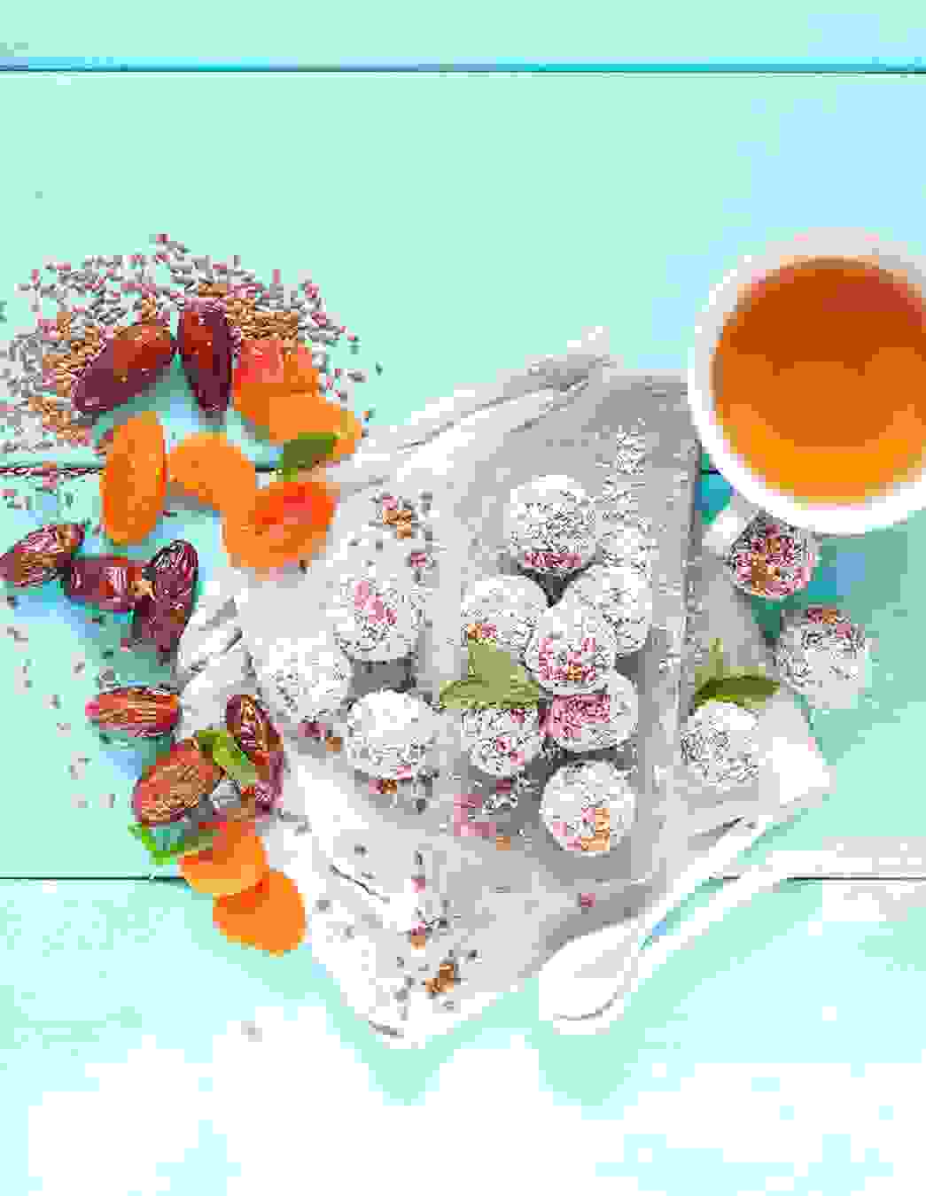 Powerballs aus Datteln, Aprikosen und Leinsamen auf einer Serviette, umgeben von einer Tasse Tee und frischen Zutaten – der ideale Snack für mehr Energie während Wochenbett und Stillzeit.