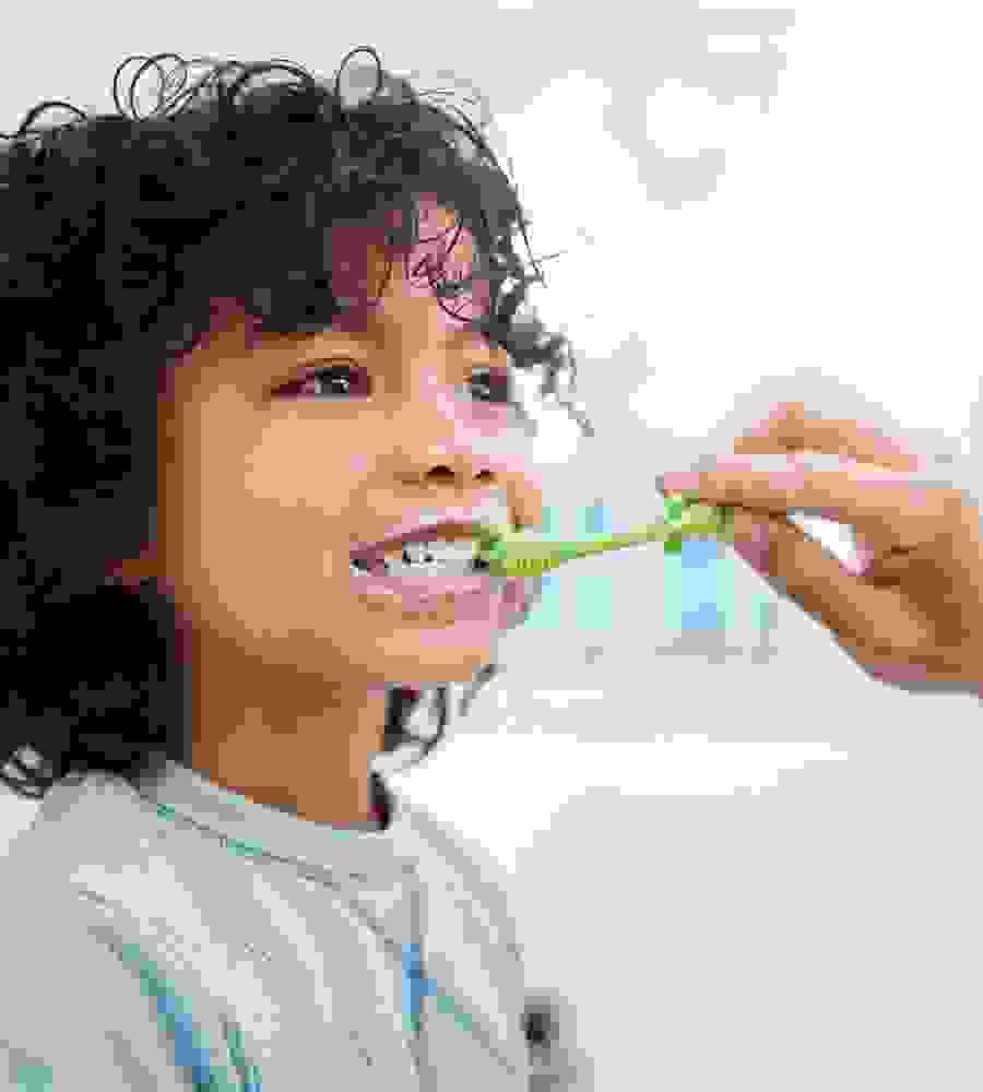 Un petit garçon se fait brosser les dents par sa mère – un moment qui montre l’importance des soins et de la santé dentaire dès le plus jeune âge.