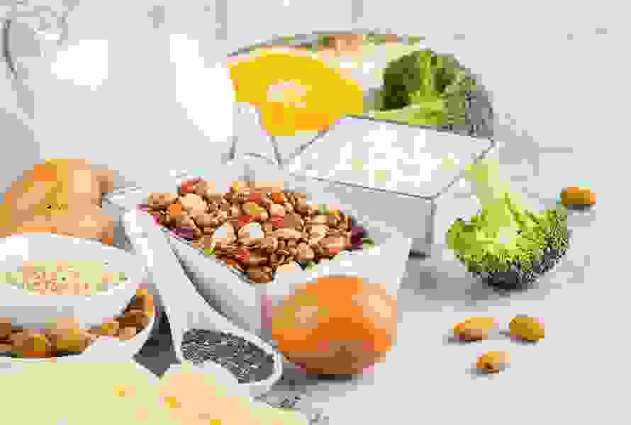 Auswahl magnesiumreicher und kalziumhaltiger Lebensmittel wie Hülsenfrüchte, Hüttenkäse, Milch, Eier, Broccoli, Chiasamen und Käse für eine ausgewogene Ernährung.