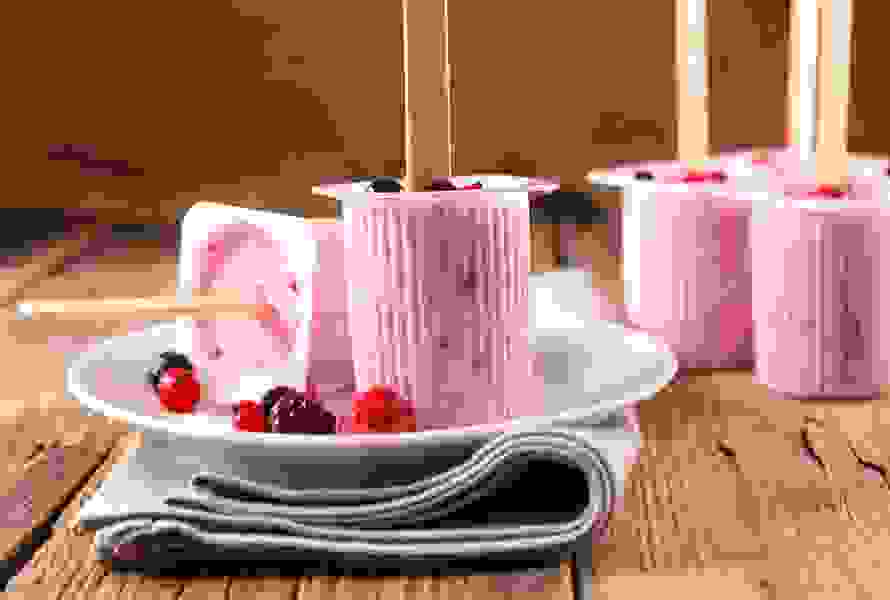 Piccoli bicchieri di yogurt con gelato allo yogurt fatto in casa e frutti di bosco freschi, su un piatto bianco con tovagliolo beige – un piacere leggero e ricco di proteine.

