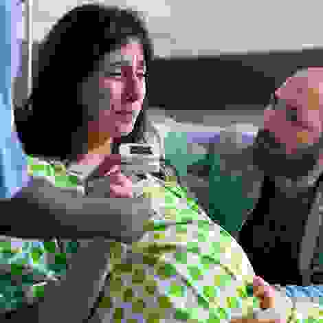 Eine Frau in den Wehen stützt sich ab, ihr Partner kniet neben ihr und gibt ihr Halt – ein emotionaler Moment kurz vor der Geburt.