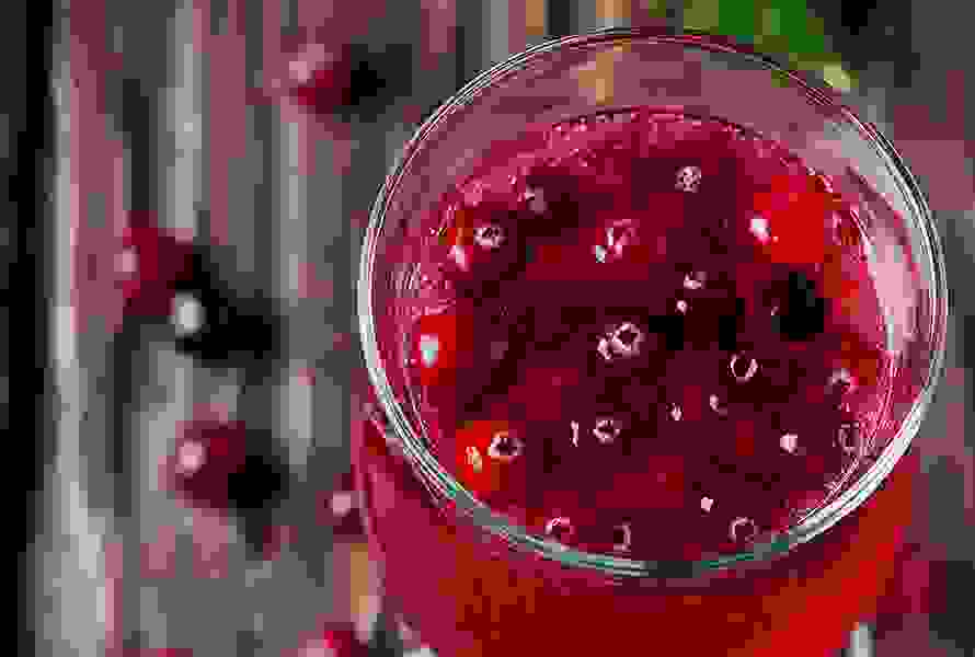 Ein Glas leuchtend roter Cranberrysaft mit frischen Cranberrys – unterstützend bei beginnender Blasenentzündung und als mildes Hausmittel in der späten Schwangerschaft.