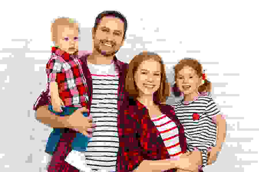 Eine Familie mit zwei Kindern steht gemeinsam vor einer weissen Backsteinwand. Ein Moment der Nähe, wie ihn PRO LIFE für alle Familien fördern möchte.