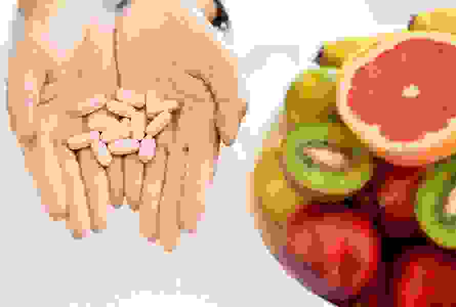 Eine Frau hält Tabletten in den Händen – daneben frisches Obst: Symbol für die Bedeutung von Folsäure und Nährstoffen in der Frühschwangerschaft.