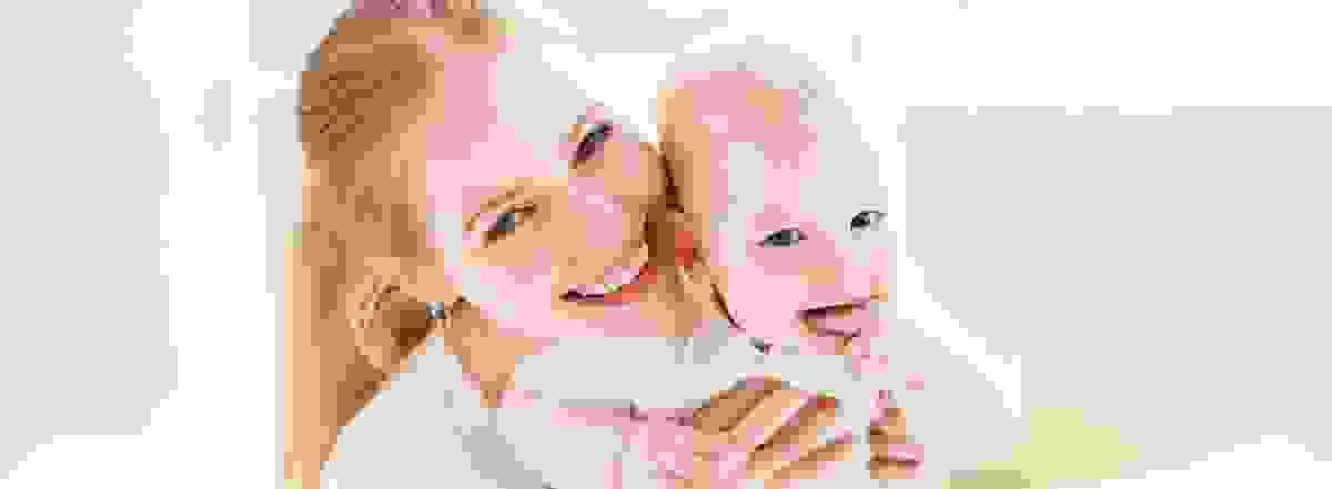 Una madre tiene amorevolmente in braccio il suo bambino piccolo. Entrambi ridono – un momento che mostra quanto sia importante la sicurezza per tutta la famiglia.