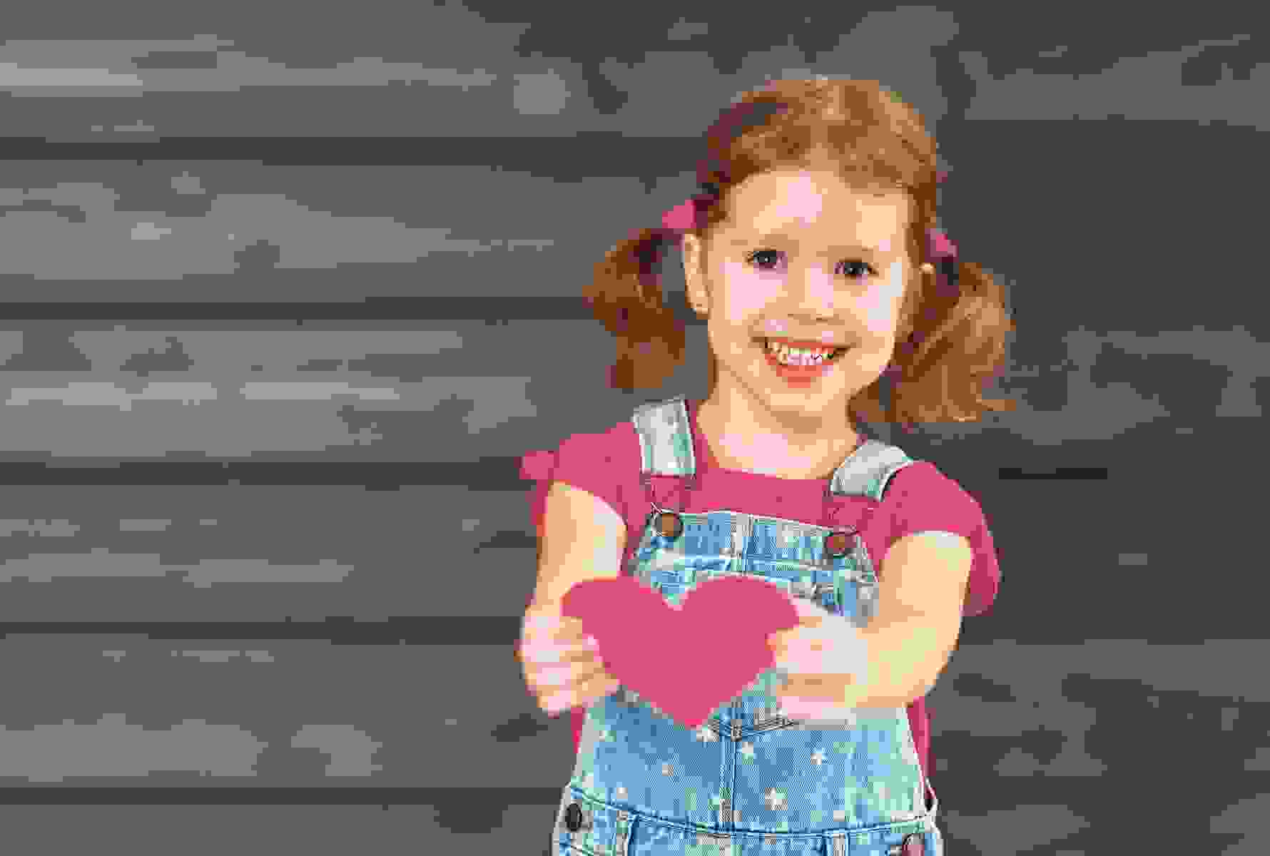 Una bambina porge un cuore verso la fotocamera – un simbolo forte di amore, cura e umanità.