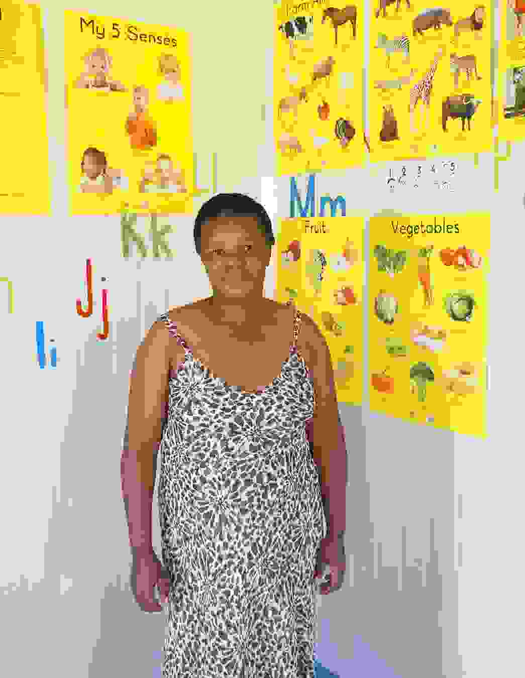 KITA-Leiterin Gladys vor bunten Unterrichtspostern – die Kinder sind begeistert vom neuen Schulalltag und kommen am liebsten täglich.