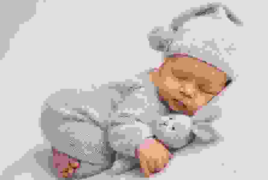 Schlafendes Baby kuschelt mit einem handgestrickten Hasen – Symbol für Geborgenheit und den neuen Lebensabschnitt.