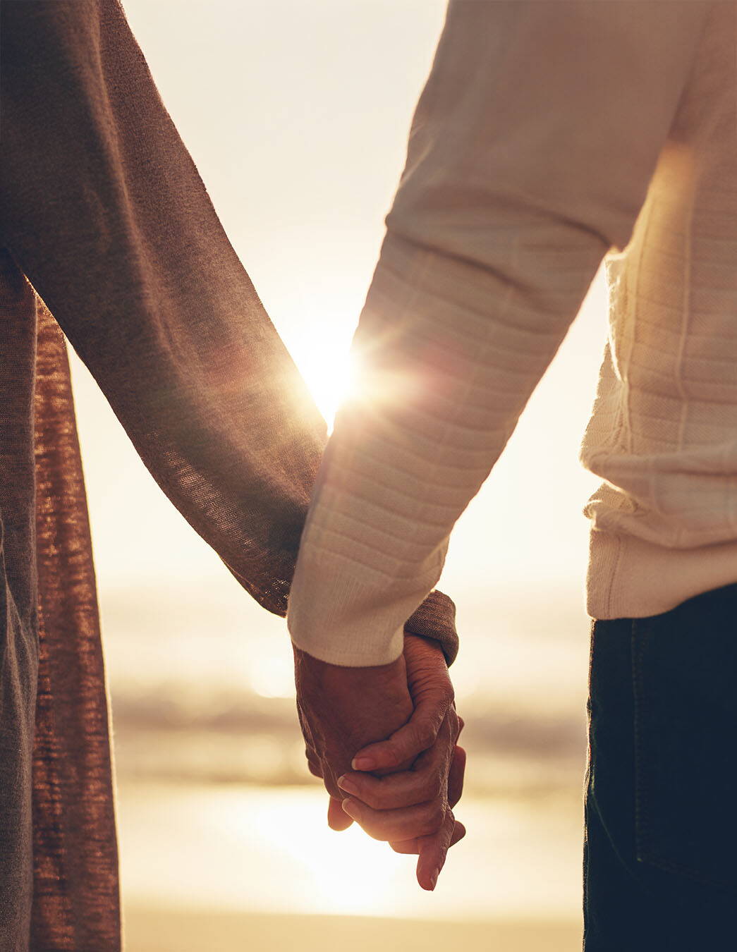 Traverser les épreuves ensemble – soutien aux familles touchées par le cancer Deux personnes se tiennent la main dans la lumière du soleil. L’image symbolise la solidarité, le soutien et l’espoir pour les familles confrontées à une maladie grave.