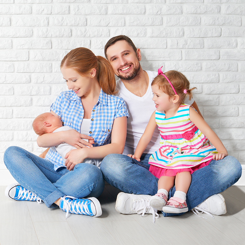 Willkommen, kleines Wunder Eine junge Familie sitzt auf dem Boden vor einer weissen Wand – zur Geburt oder Adoption erhalten Sie unter bestimmten Voraussetzungen CHF 400.– als Geschenk.