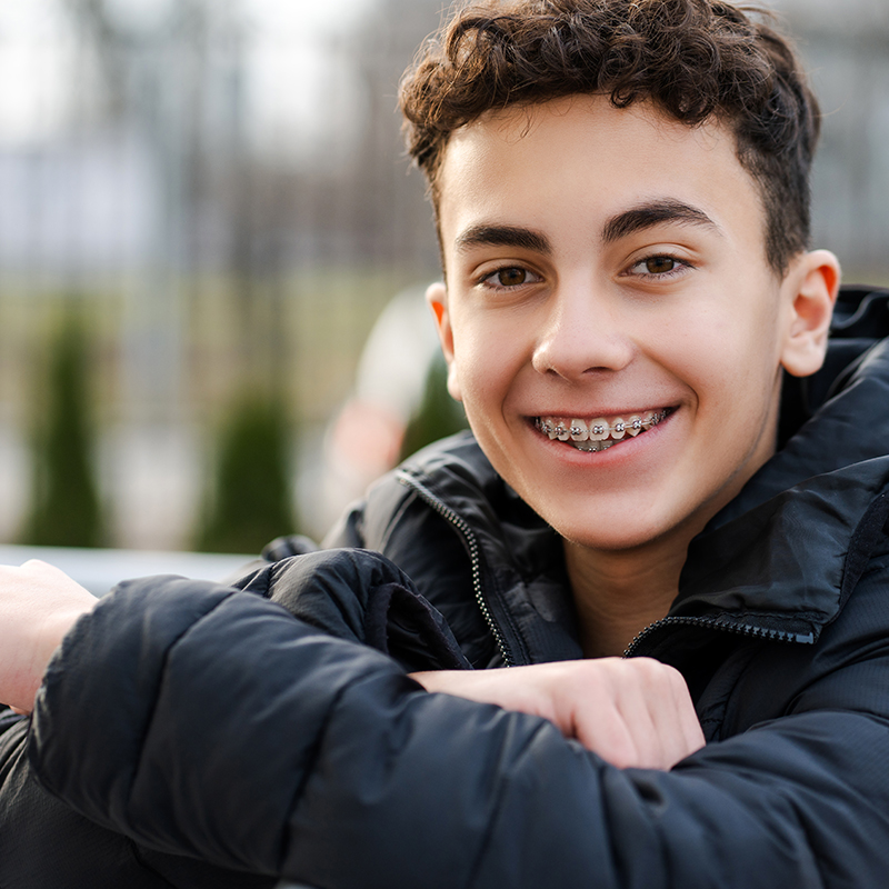 Un adolescent avec un appareil dentaire sourit à la caméra – PRO LIFE prend en charge jusqu’à 90 % des coûts des traitements orthodontiques.