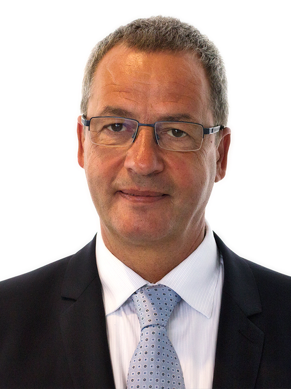 Thomas Seitz Ritratto professionale in abito scuro con cravatta azzurra a motivi su sfondo neutro.