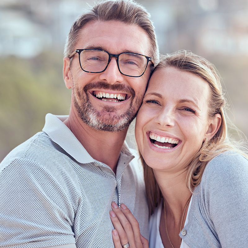Deux personnes se tiennent proches l’une de l’autre et portent des vêtements clairs. L’arrière-plan montre un paysage flou, suggérant une scène en plein air.