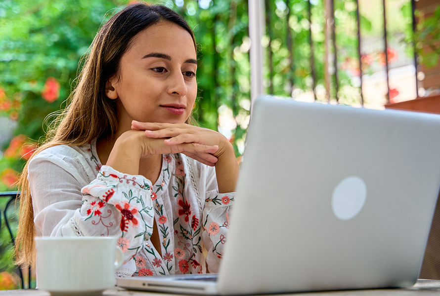 Contattarci è facile Una giovane donna è seduta rilassata sul balcone e utilizza il formulario online – veloce e comodo.